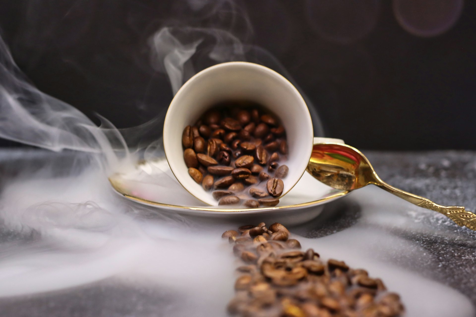 Coffee beans spilling from an overturned cup with steam.